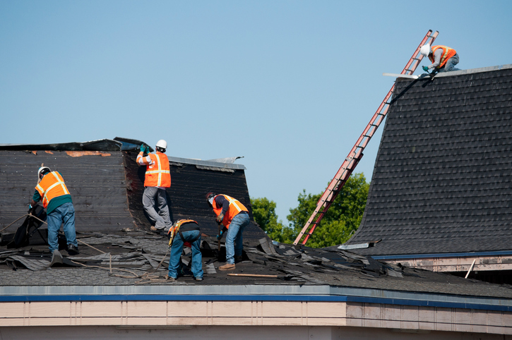 A crew of construction workers putting new shingles on a house.