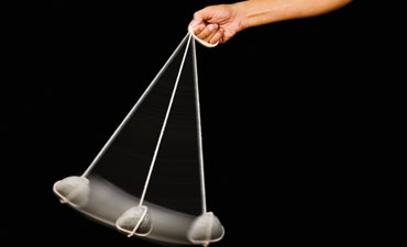 A hand swinging a stone pendulum.