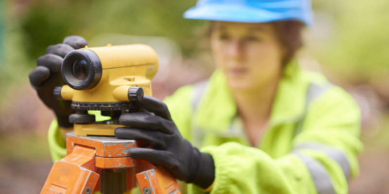 A construction worker uses a spirit level to make sure her surveying equipment is parallel to the ground