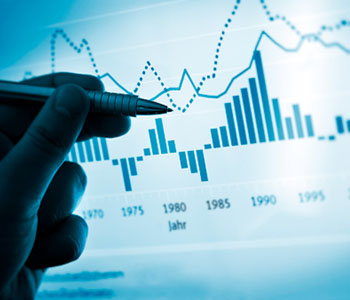 A person holding a pen up to a chart with high peaks and low peaks.