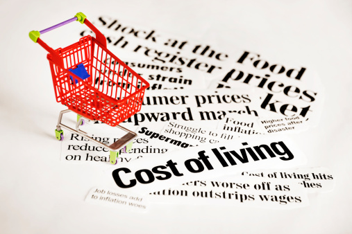 Shopping cart with news headlines regarding inflation cut out surrounding the cart.