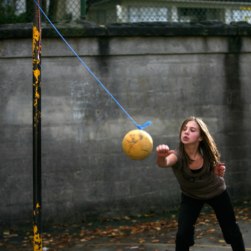 Tetherball has a ball on a string attached to the top of a tall pole where people take turns hitting the ball around the pole.