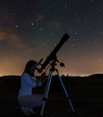 A woman looking through a telescope at the night sky,